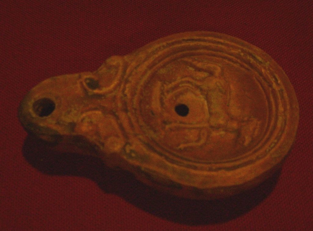 Lucerna (rzymska lampka oliwna) z terakoty z szarawą patyną i twarzą boga z porożami